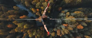 An overhead view of someone walking on a tightrope high above a forest.